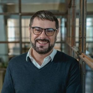 Smiling man in glasses posing at the camera while standing with mobile phone in a modern workplace